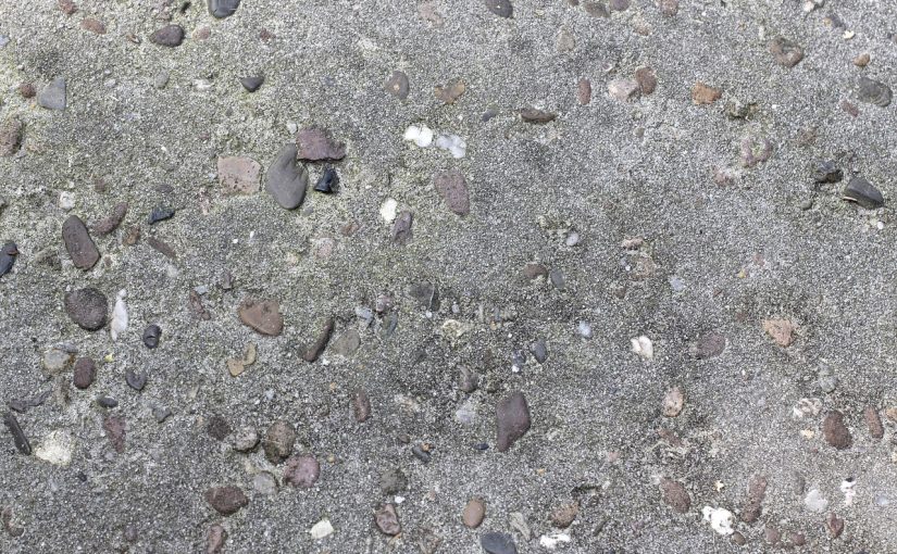 Szara betonowa powierzchnia podłogi z widocznym kruszywem i drobnymi kamykami.